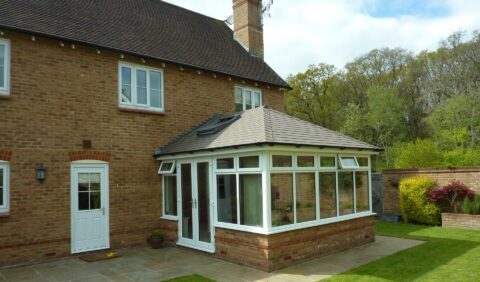 A conservatory featuring a white roof and a patio, surrounded by greenery and natural light.