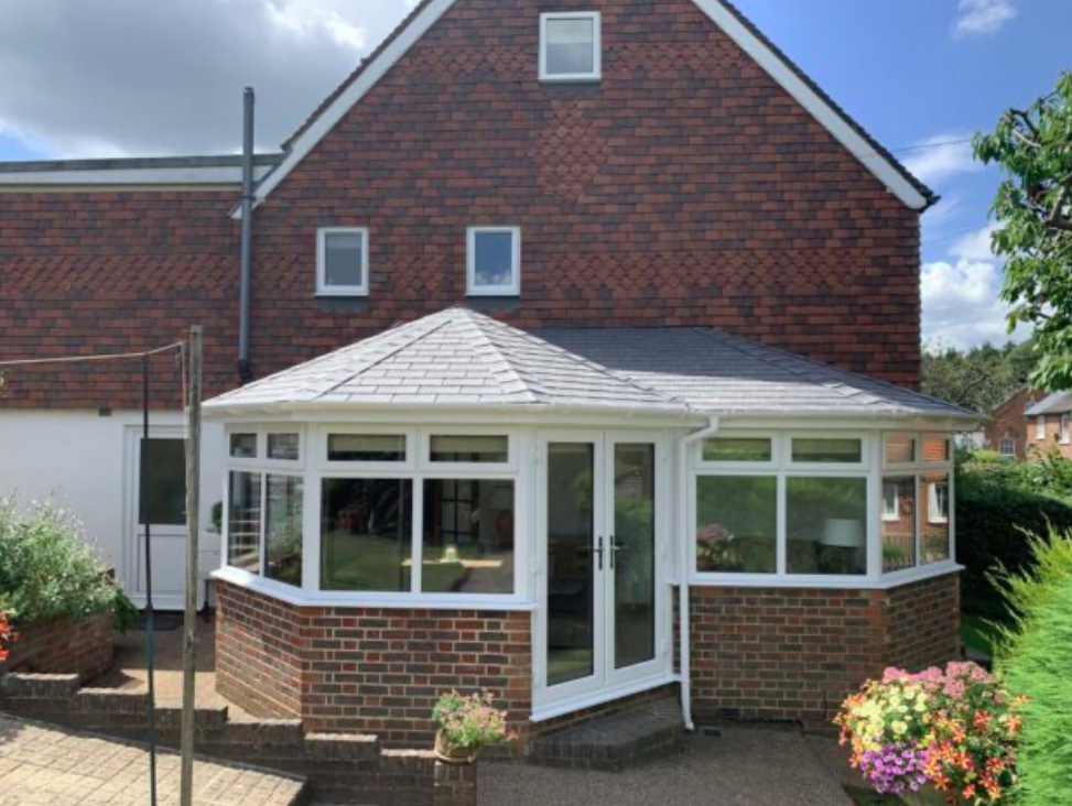 A house featuring a large patio, a roof, and a conservatory, surrounded by greenery.